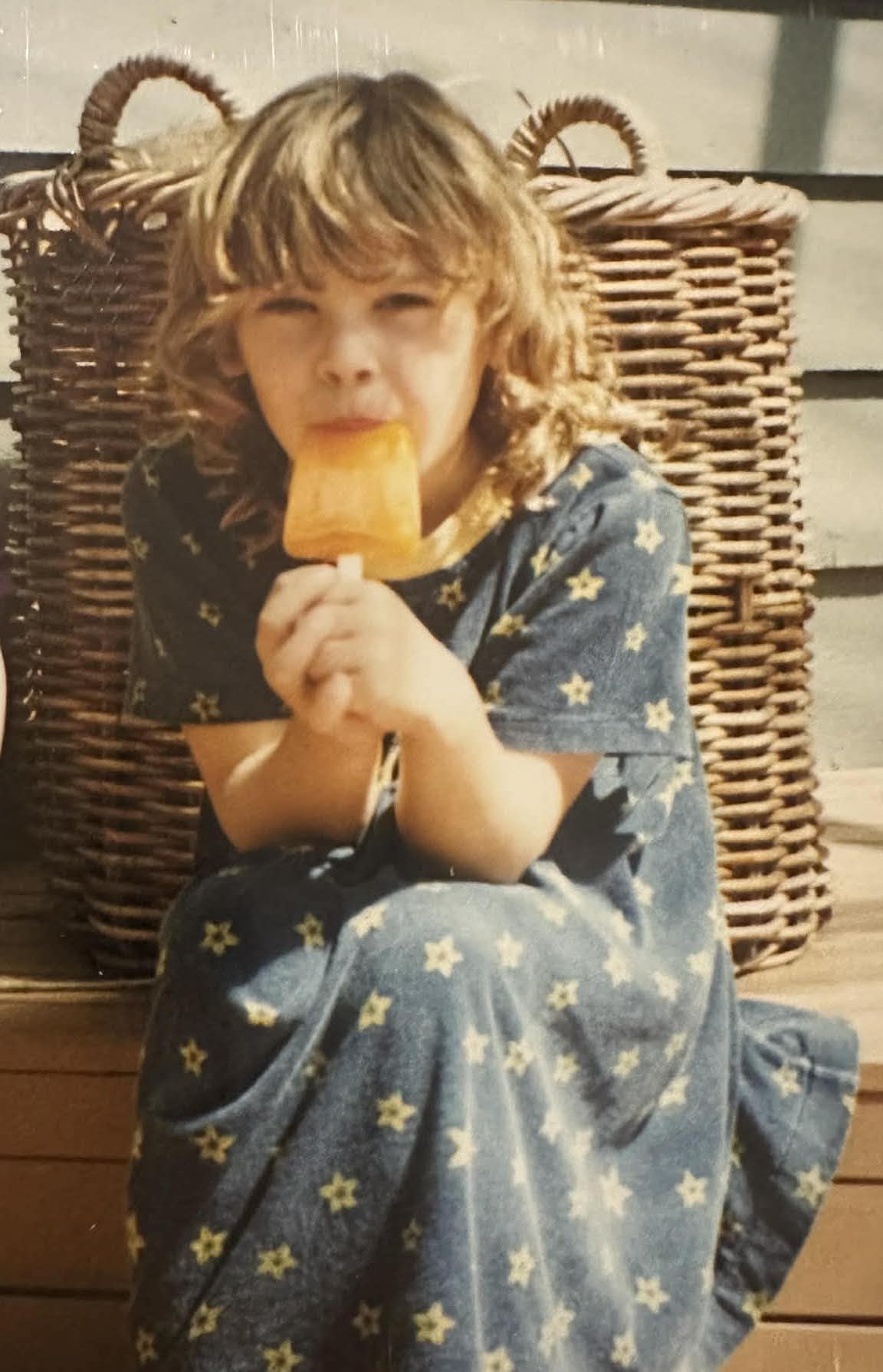 Child eating an orange icy pole outdoors beside wicker baskets